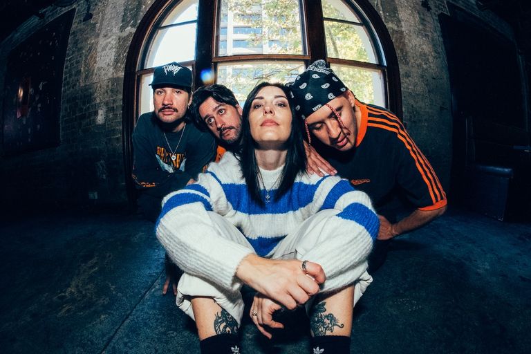 Australian pop-punk band Stand Atlantic posing indoors in front of an arched window with vocalist Bonnie Fraser sitting in front.